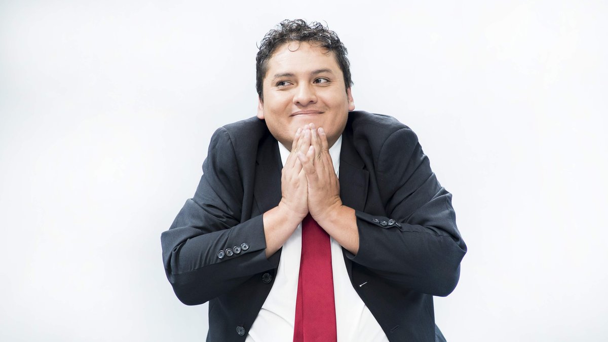 Wilson Tituaña con traje y corbata roja, las manos juntas y una sonrisa cómplice.